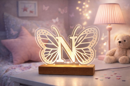 Butterfly-shaped night light with letter 'N' on a wooden base in a cozy room setting.