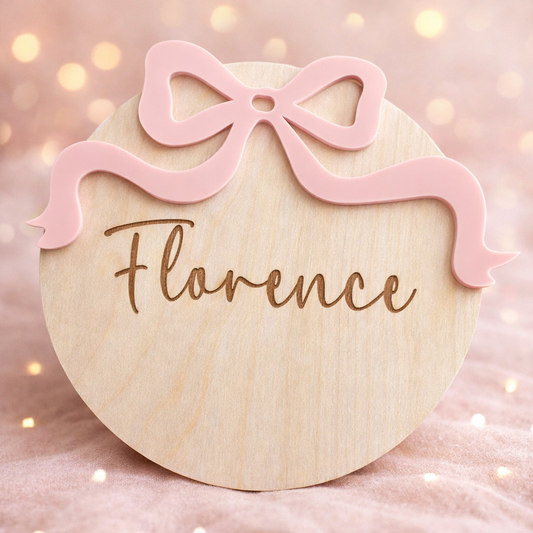 Wooden round plaque with pink bow and engraved name 'Florence' on a soft pink background