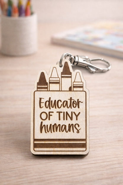 Wooden keychain with 'Educator of Tiny Humans' text and crayon design on a wooden surface.