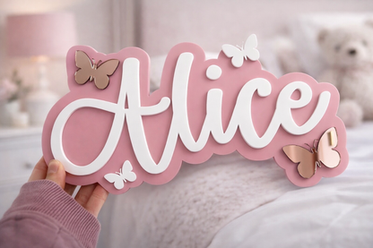 Pink decorative sign with 'Alice' and butterflies held by a hand against a blurred indoor background