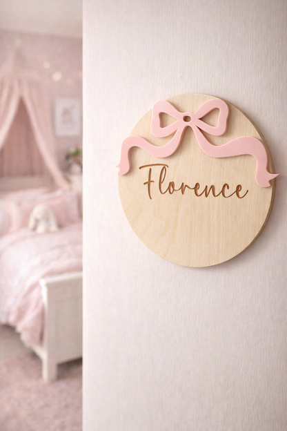 Round wooden plaque with pink bow and 'Florence' text in a bedroom setting