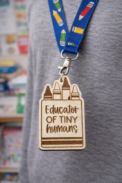 Laser-cut wooden badge with 'Educator of Tiny Humans' text and crayon design on a blue lanyard.